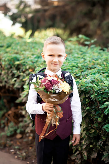 Full length of boy holding flower standing against plants