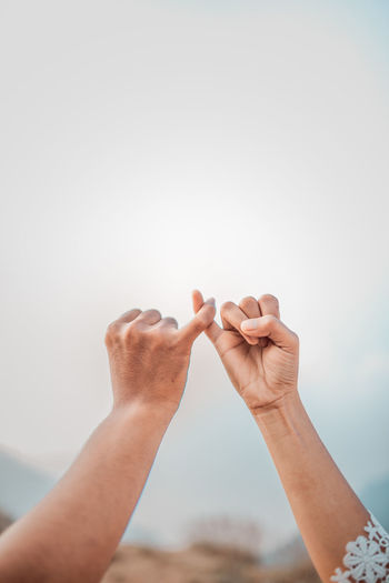 Cropped hand of couple holding little fingers against clear sky