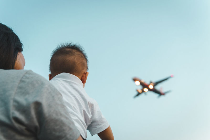 Rear view of young boy and airplane flying against clear sky