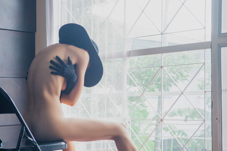 Naked seductive woman sitting on chair by window at home