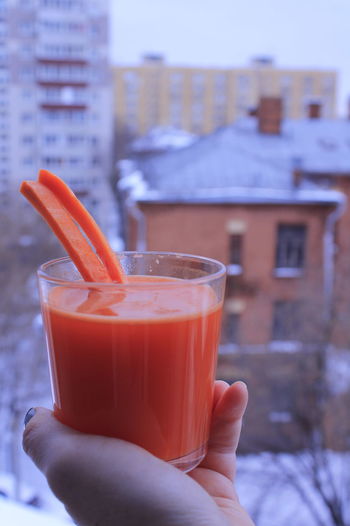 Cropped hand holding drink carrot juice on the background of winter city