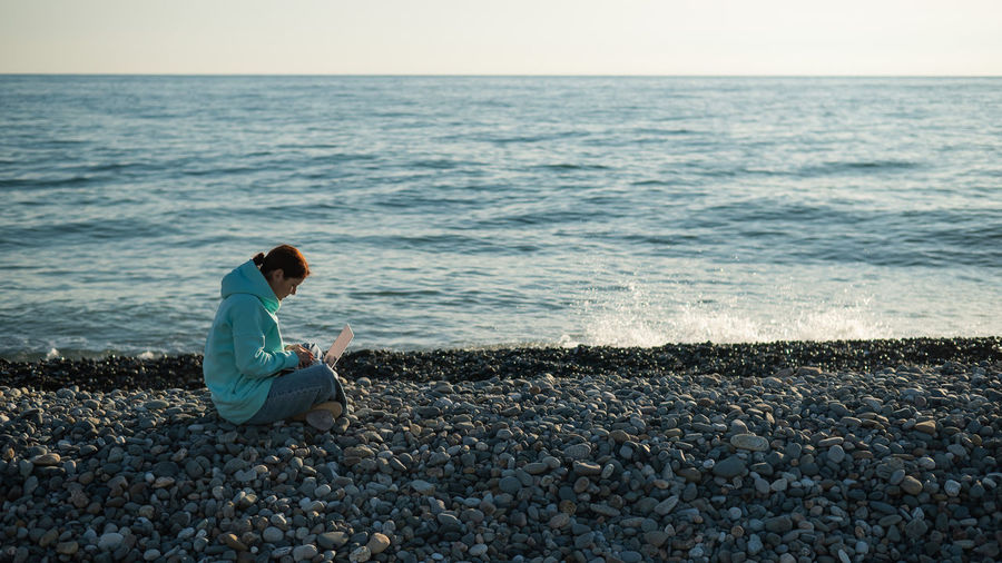 Side view of woman using laptop at beach