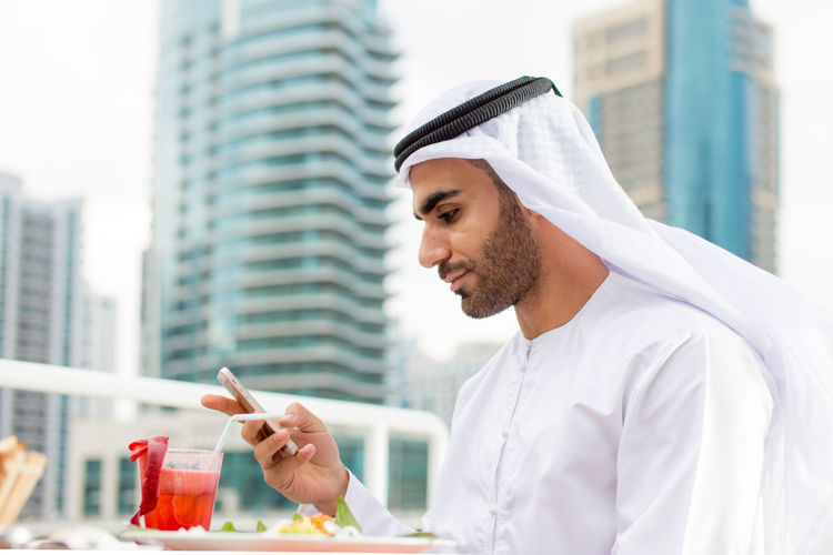 Man in traditional clothing using smart phone at outdoor restaurant