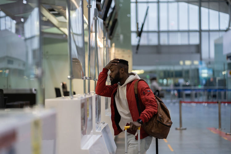 Upset african student guy in airport feeling uncertain about moving to another country