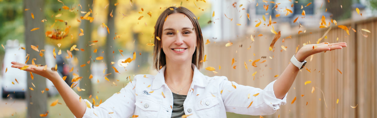 Portrait of young woman throwing leaf outdoors