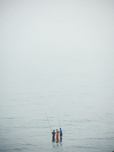 Men fishing in sea against sky