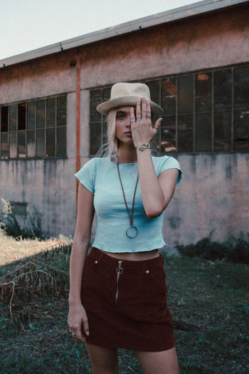Portrait of young woman wearing hat standing against built structure