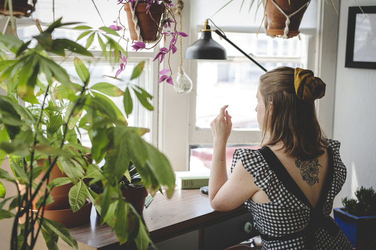 Young woman sits at desk with plants and books