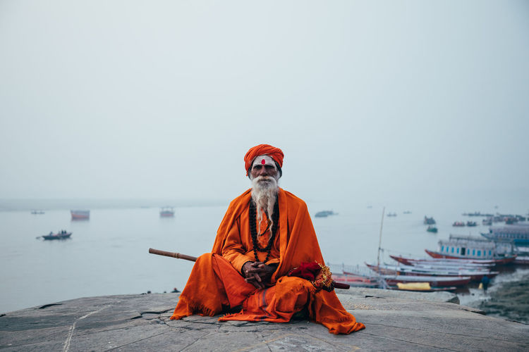 Varanasi, india - february, 2018: aged bearded hindu male in orange turban sitting on street and looking at camera