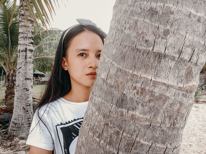 Portrait of woman standing by tree trunk