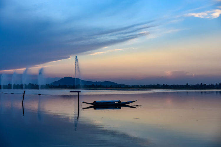 Silhouette boat in dal lake against sky during sunset in srinagar.