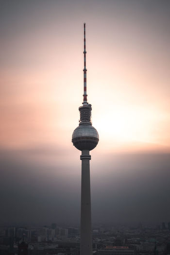 Communications tower in city against romantic sky at sunset