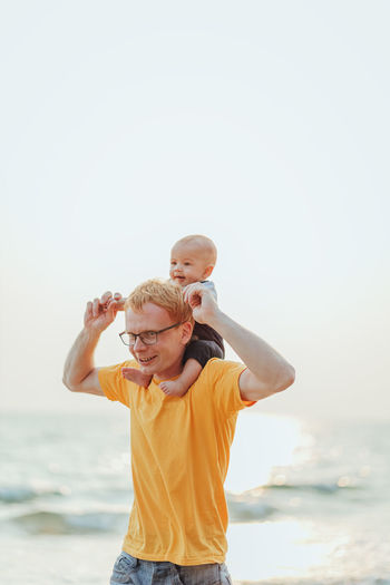 Father carrying son on shoulders at beach against clear sky
