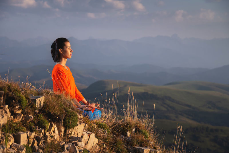 Meditating woman with closed eyes in bright clothes in the mountains, sportswear advertising banner
