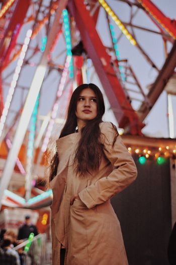 Low angle view of beautiful woman standing against illuminated ferris wheel