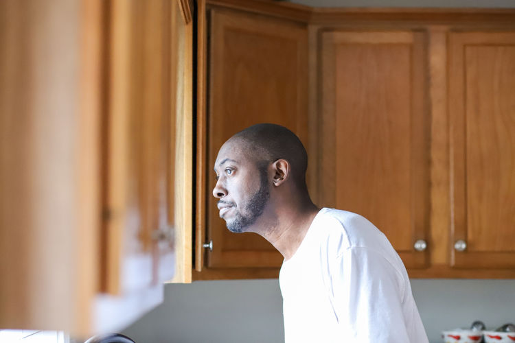 A portrait of a african-american man looking out of a kitchen window