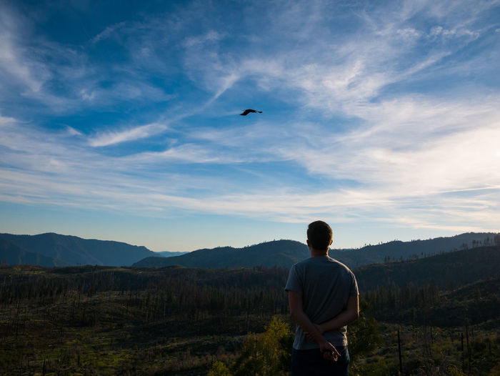 Rear view of man standing on mountain against sky