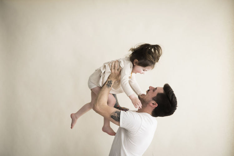 Happy millennial hipster father holds toddler girl above his head