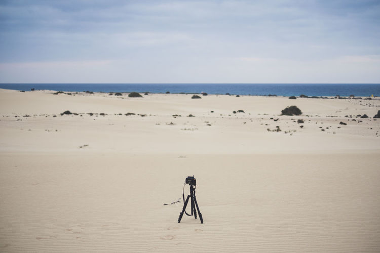 Camera on sand at beach against sky