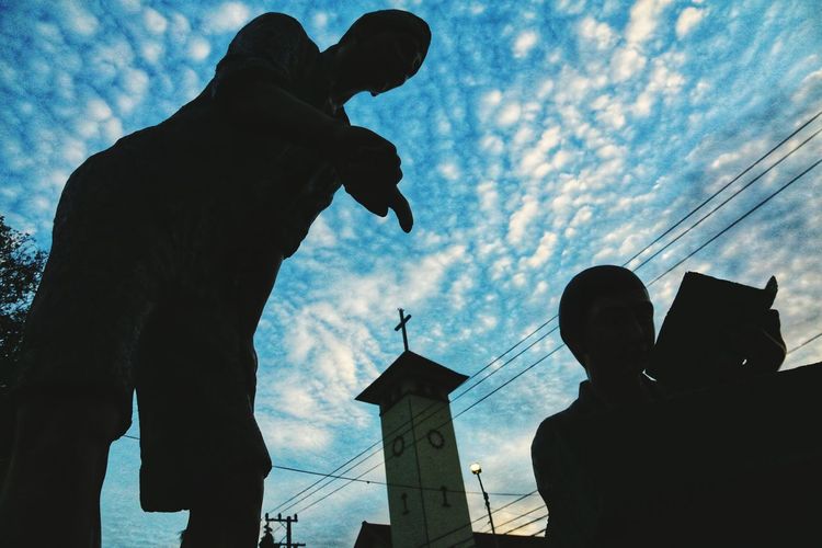 Low angle view of silhouette statue against building against sky