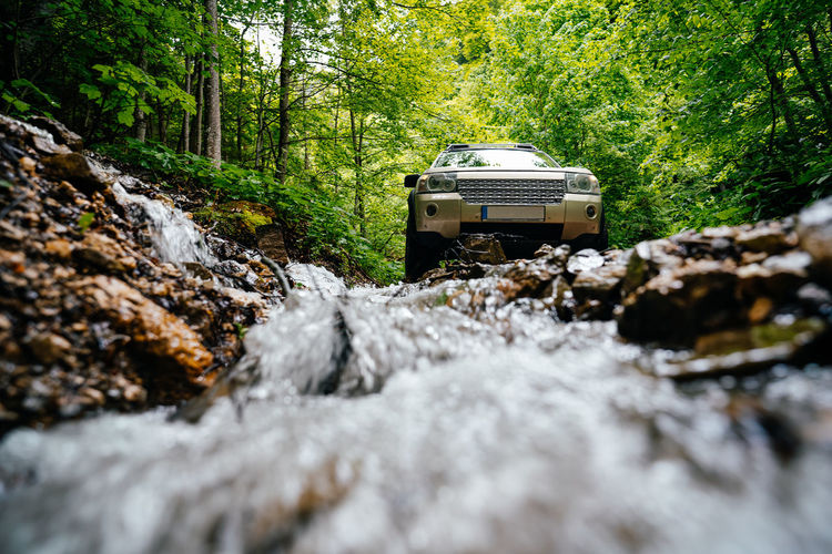  suv car by stream flowing through rocks in forest
