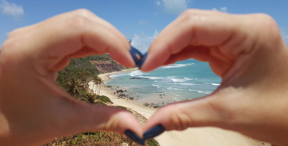 Cropped image of woman making heart shape with hands against beach