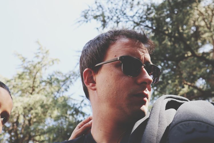 Low angle view of young man wearing sunglasses by woman against trees