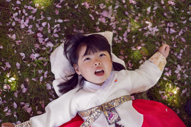 Korean girl child in a national costume lies on the back in a garden with cherry blossoms in spring