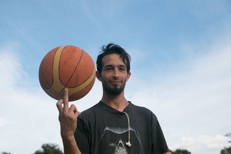 Portrait of young man with basketball against sky