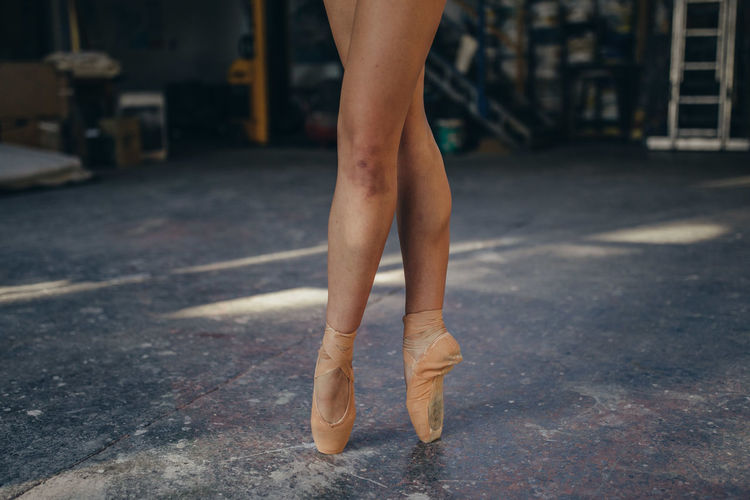 Crop unrecognizable female ballet dancer in pointes with bruise on leg standing on tiptoe while performing classic exercise during training in studio