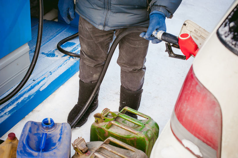 Low section of man refueling car with fuel pump during winter