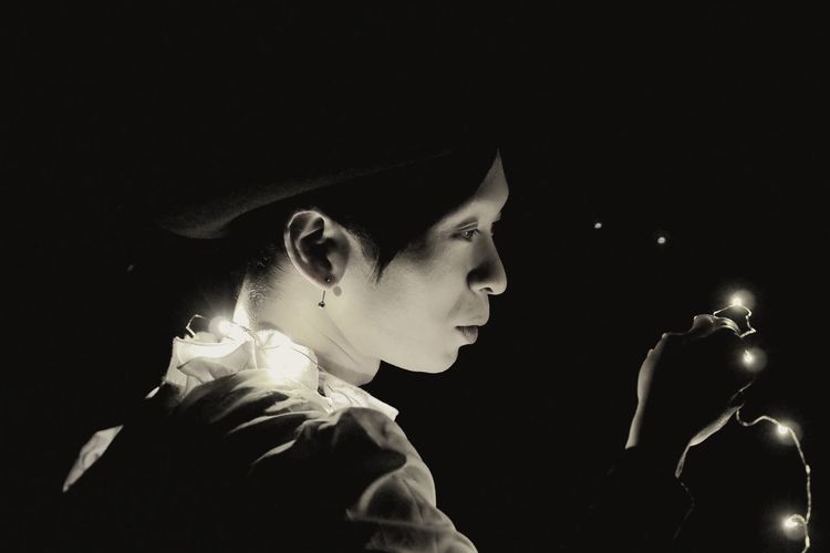 Side view of woman holding illuminated string light in darkroom