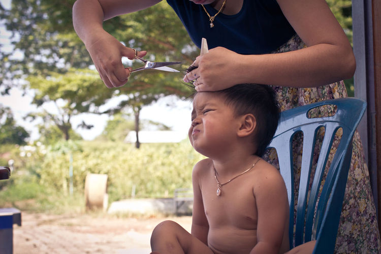 Midsection of woman cutting boy hair sitting on chair