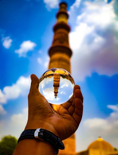 Cropped hand of man holding crystal ball against tower