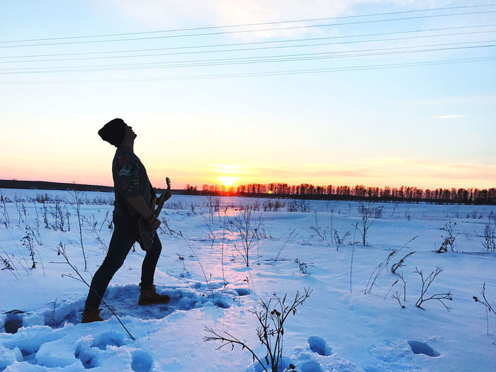 Man standing on snow covered field against sky during sunset
