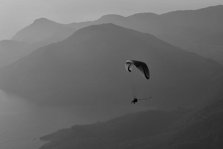 Distant view of person paragliding over mountains during sunset