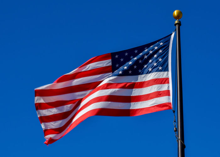 Usa flag  in red white and blue with stars and stripes blowing in the wind on brass flagpole 