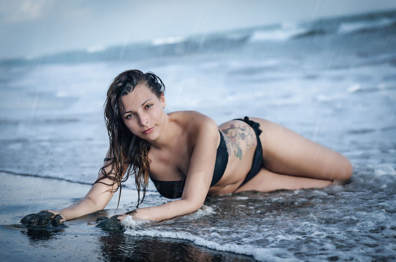 Portrait of sensuous woman wearing bikini while shore during rainy season