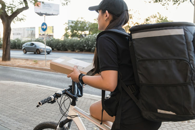 Female frontline worker delivering box while riding bicycle