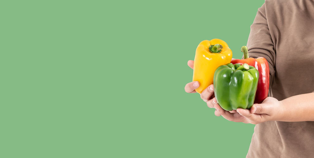 Midsection of man holding bell pepper against green background