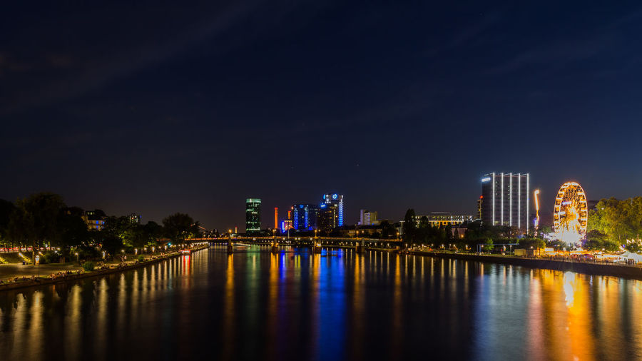 Illuminated city by river against sky at night