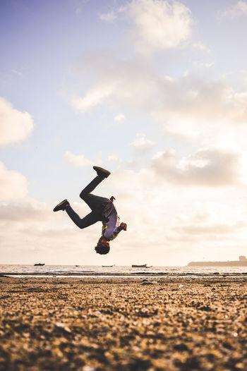 Full length of man jumping at beach against sky