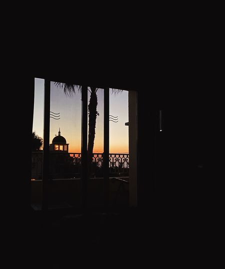 Silhouette building against sky during sunset seen through window