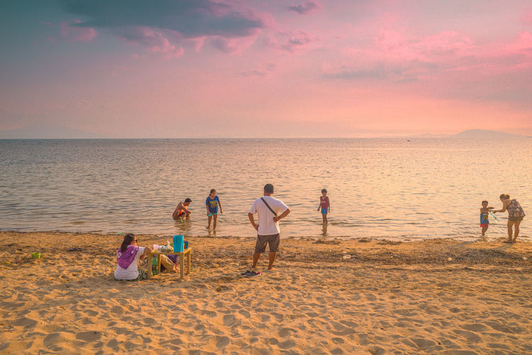 People playing on beach against sky during sunset