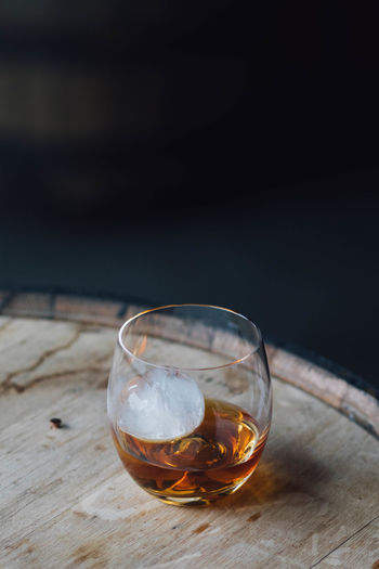 Close-up of whiskey in glass with ice sphere on bourbon barrel 