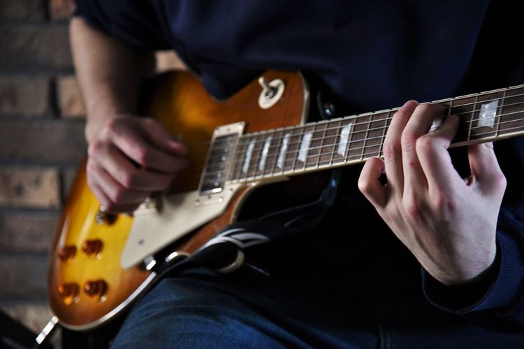 Midsection of man playing guitar while sitting on seat