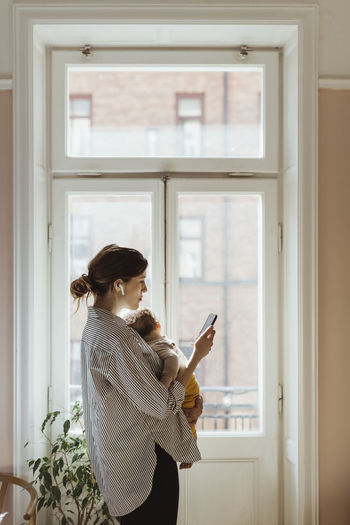 Mother using smart phone while carrying baby boy at home