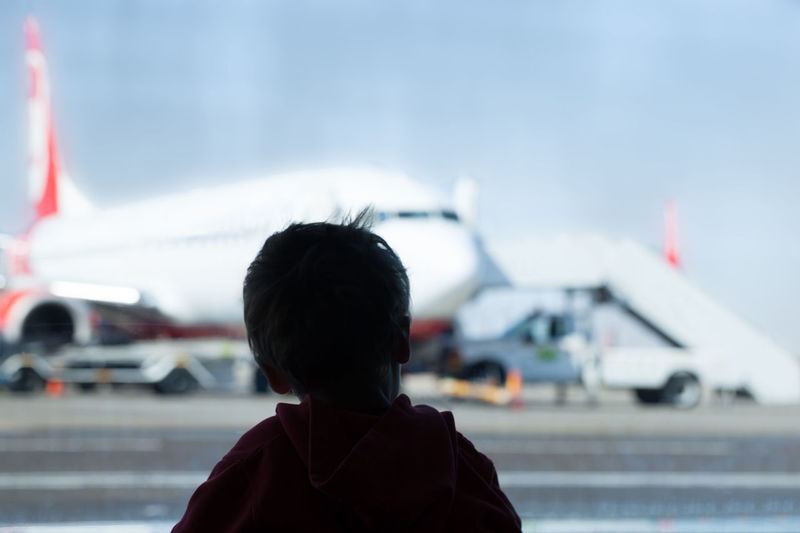 Rear view of boy against airplane at airport