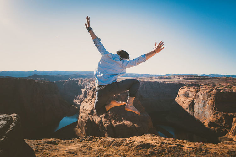Man jumping on rock by mountain against sky