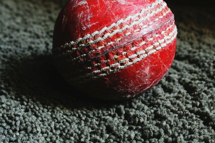 Close-up of red cricket ball on rug at home